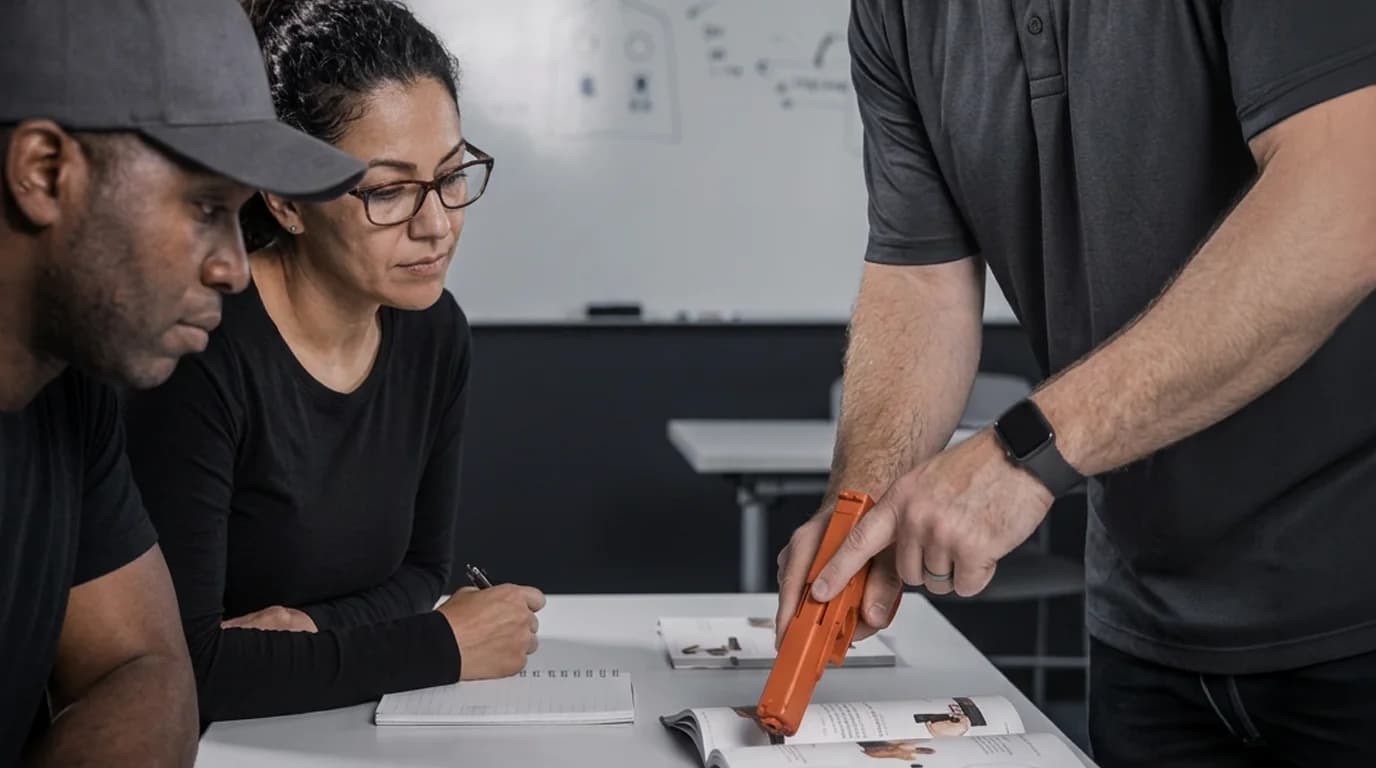 Firearm instructor pointing out a detail in the training manual to two learners in a classroom